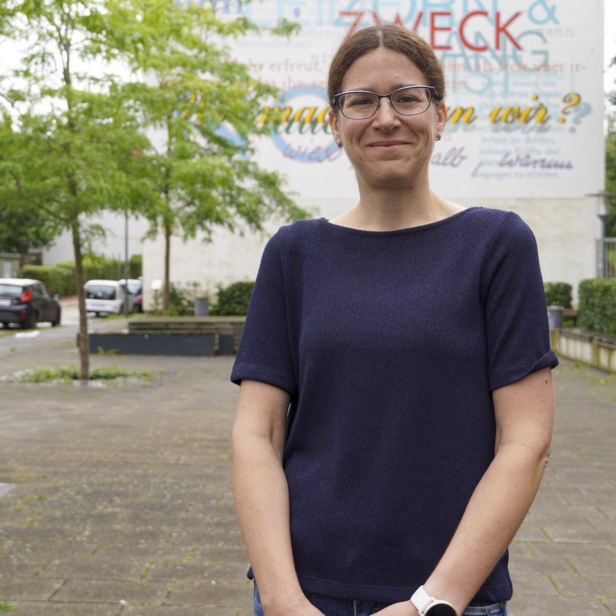 Prof. Dr. Anna Isenhardt steht vor einem Wandgemälde auf dme Campus der FH Kiel. 