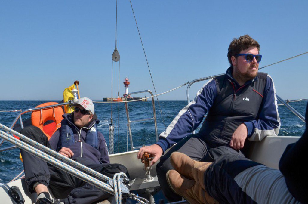 Zwei Männer sitzen entspannt am Heck eines Segelbootes und genießen die Fahrt.