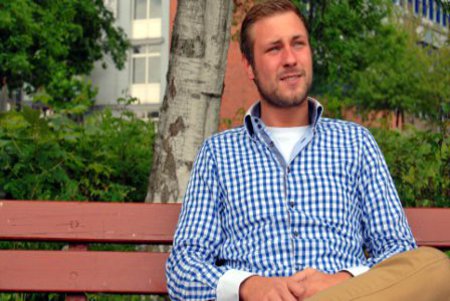 Sascha Blunk vor der Fachhochschule Kiel, auf einer Bank sitzend