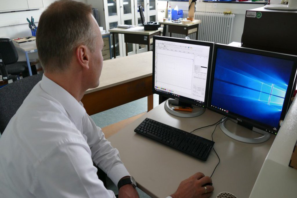 Ein Mann in weissem Hemd sitzt an einem Computer mit zwei Monitoren.