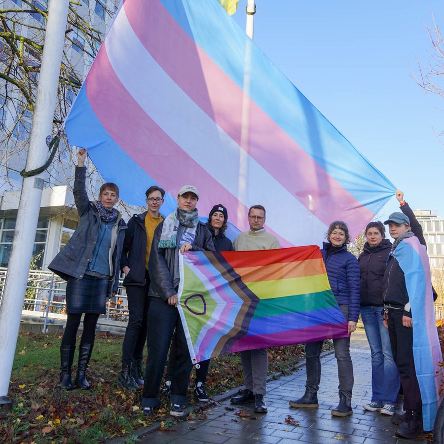 Mitglieder der FH Kiel stehen an Fahnenmasten und hissen die Trans*-Fahne   