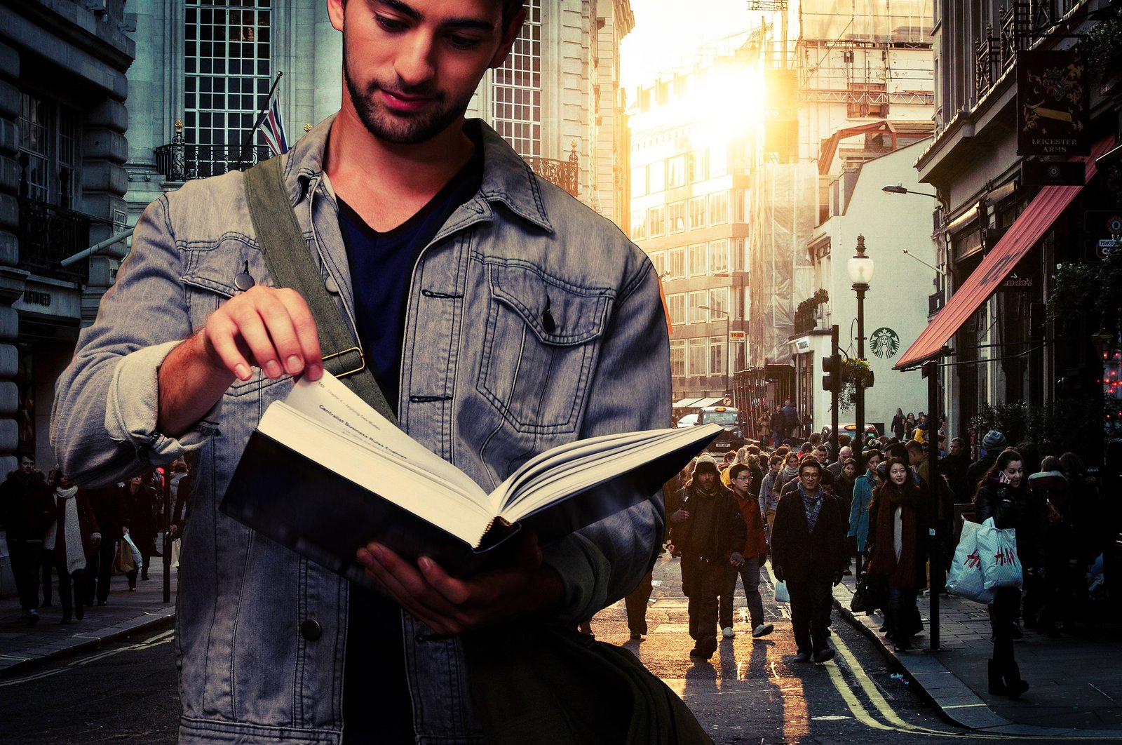 Ein mit Jeansjacke und Umhängetasche bekleideter Mann hält ein aufgeschlagenes Buch in den Händen. Hinter ihm sind viele Menschen zu sehen, die sich in einer Großstadt bewegen.