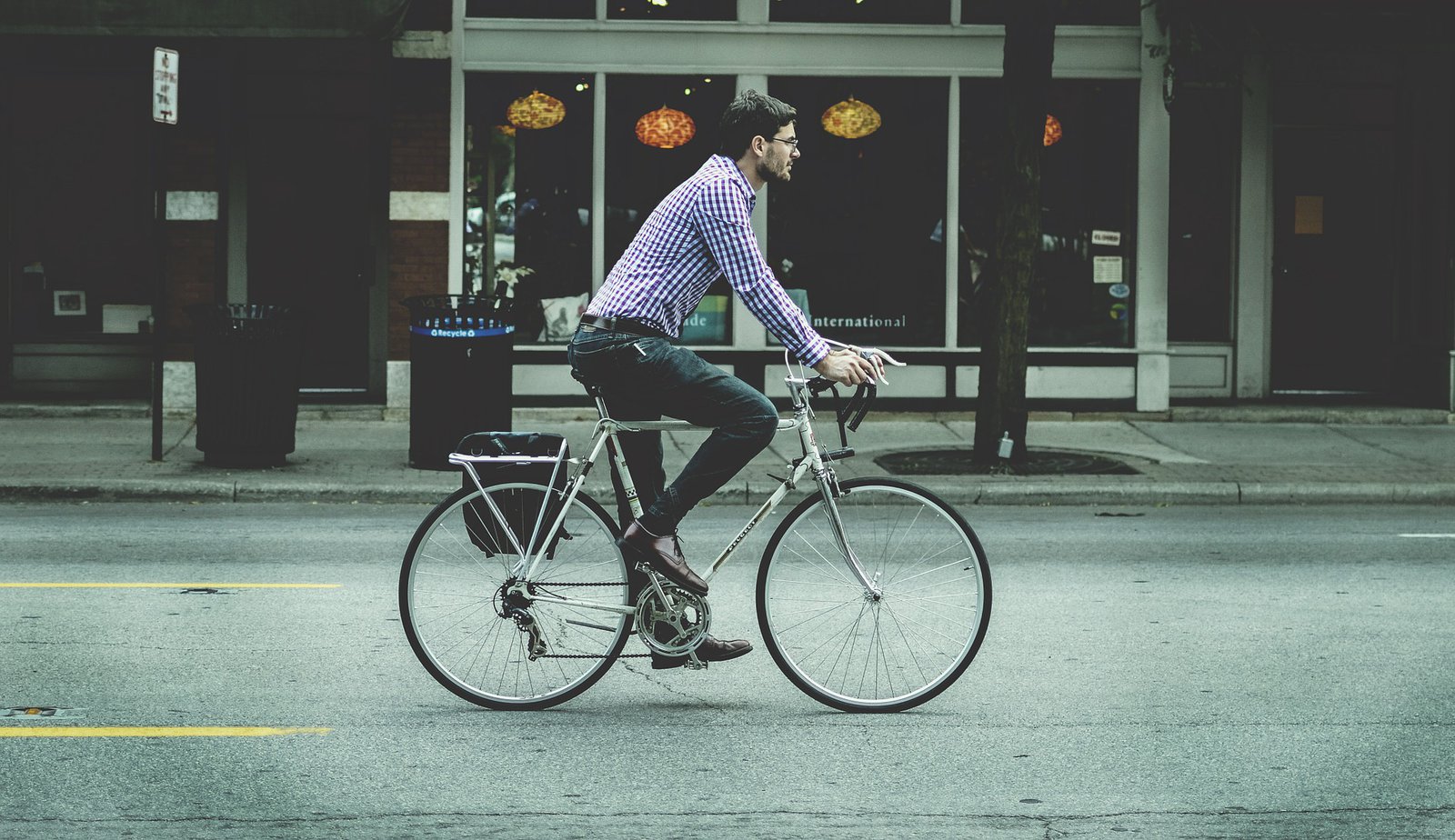 Ein Mann in kariertem Hemd, fährt auf seinem Fahrrad über eine leere Straße.