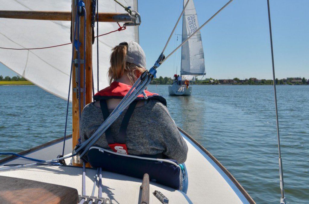 Eine Person lehnt sich an den Mast eines Segelbootes an und genießt die Fahrt.