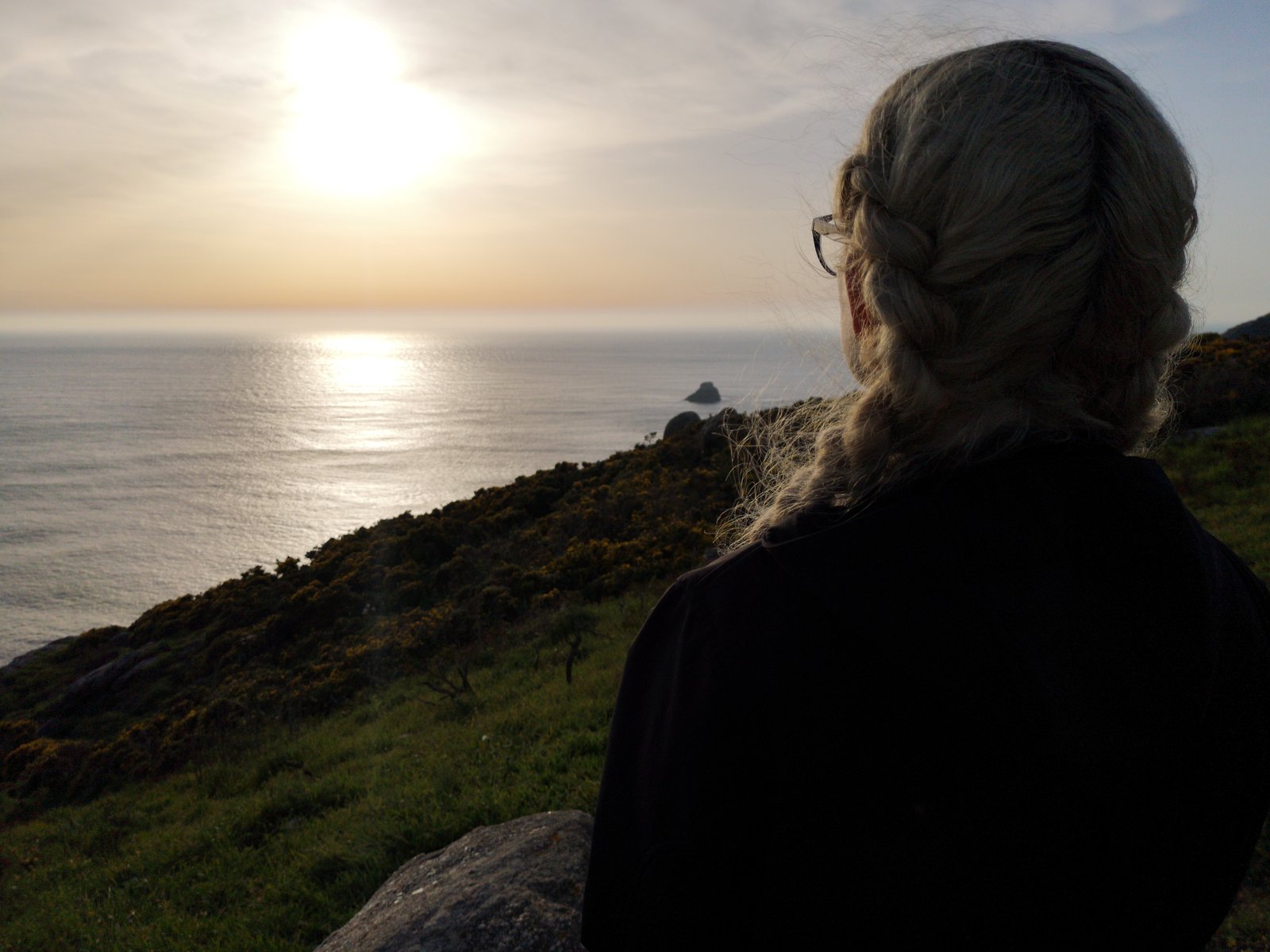 Eine Frau steht an einem Abhang und betrachtet die über dem Meer aufgehende Sonne.