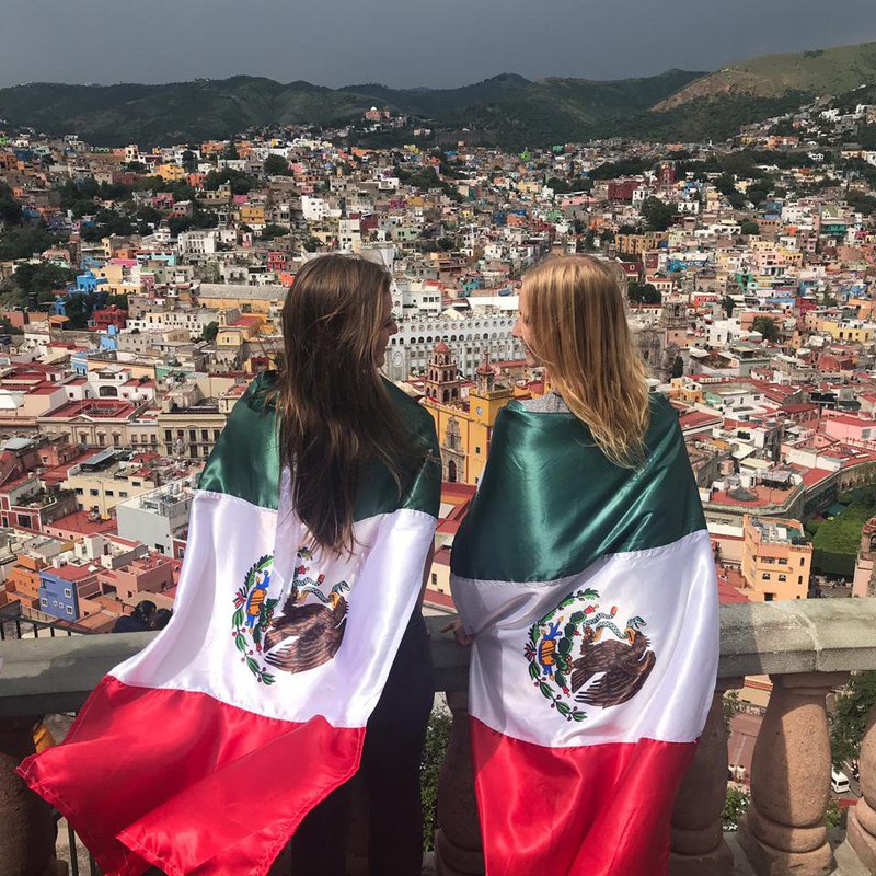 Zwei Frauen mit mexikanischer Flagger blicken auf eine Stadt