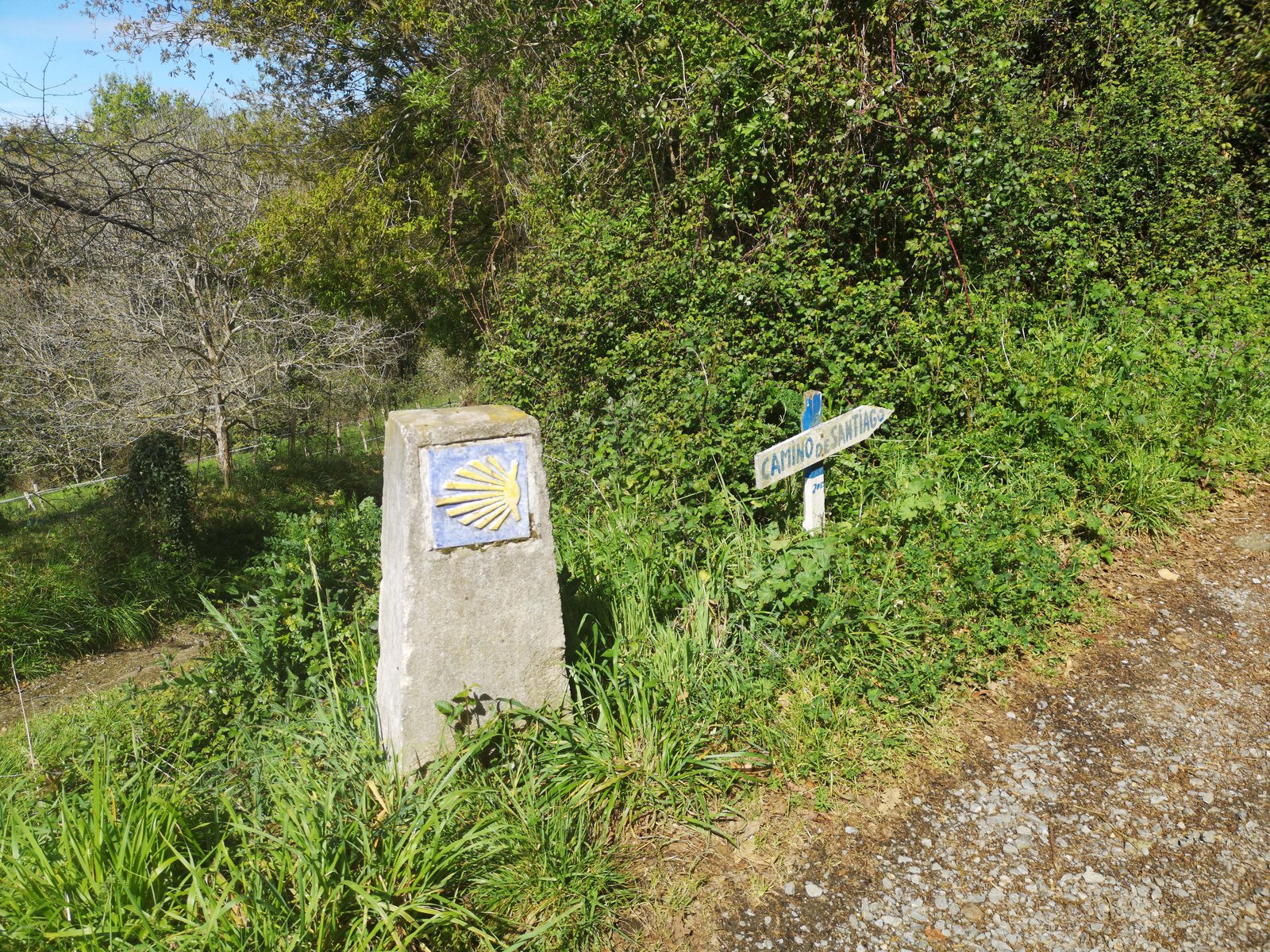 Ein Stein mit einem gelben Muschelsymbol und ein Wegweiser am Wegerand.