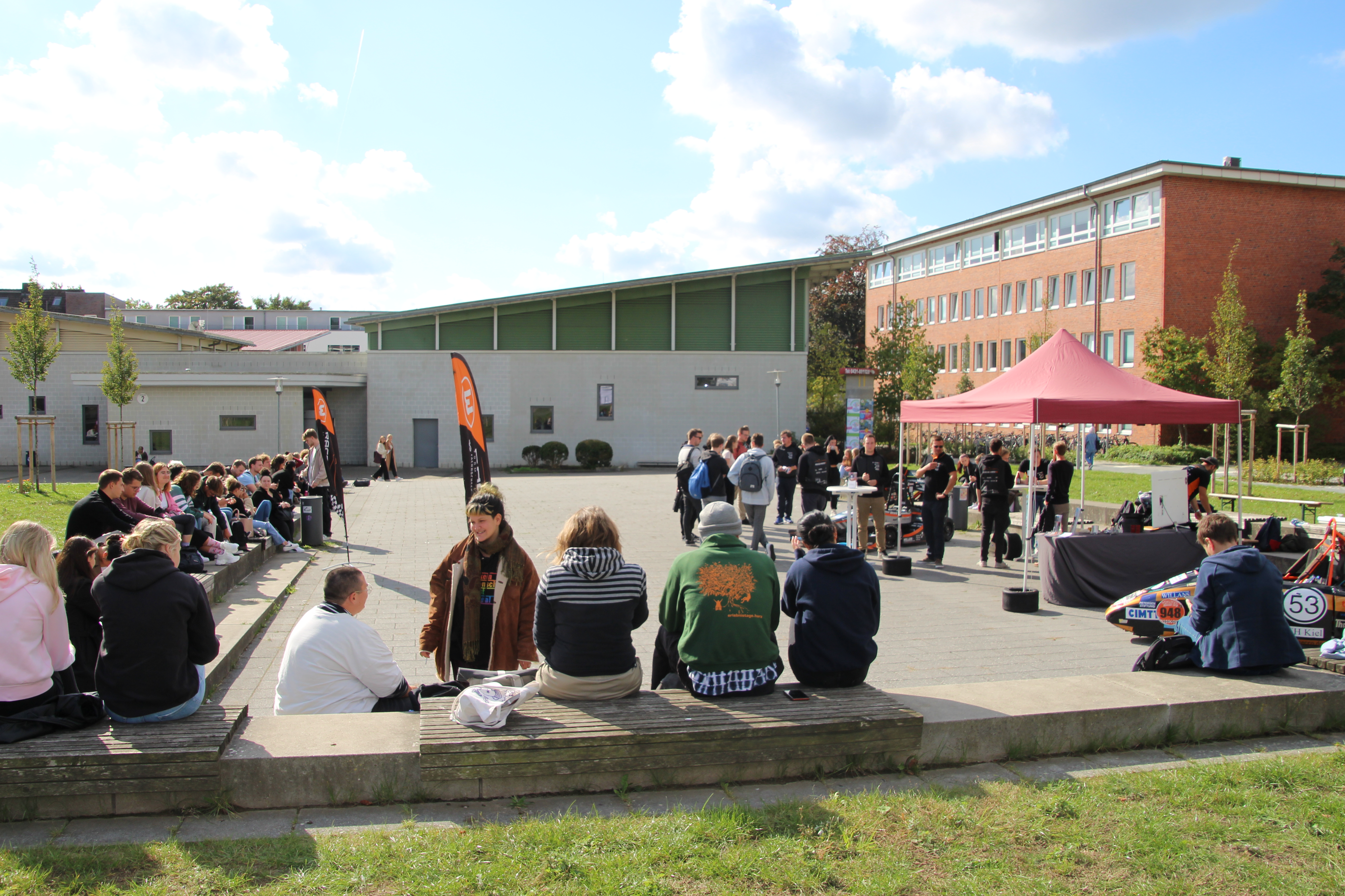 Junge Menschen sitzen in Gruppen zusammen um einen Platz herum