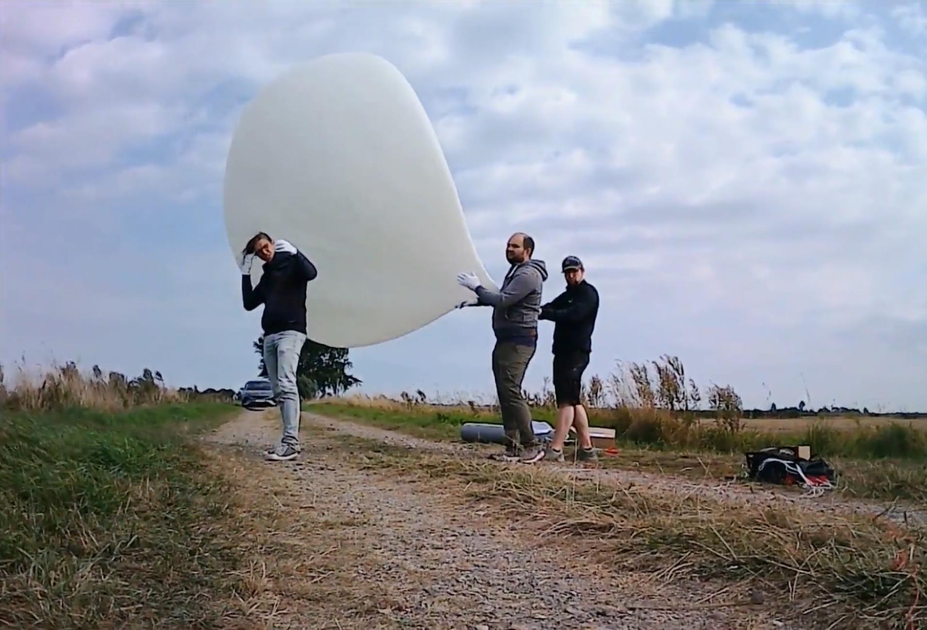 drei Menschen auf freiem Feld mit Wetterballon