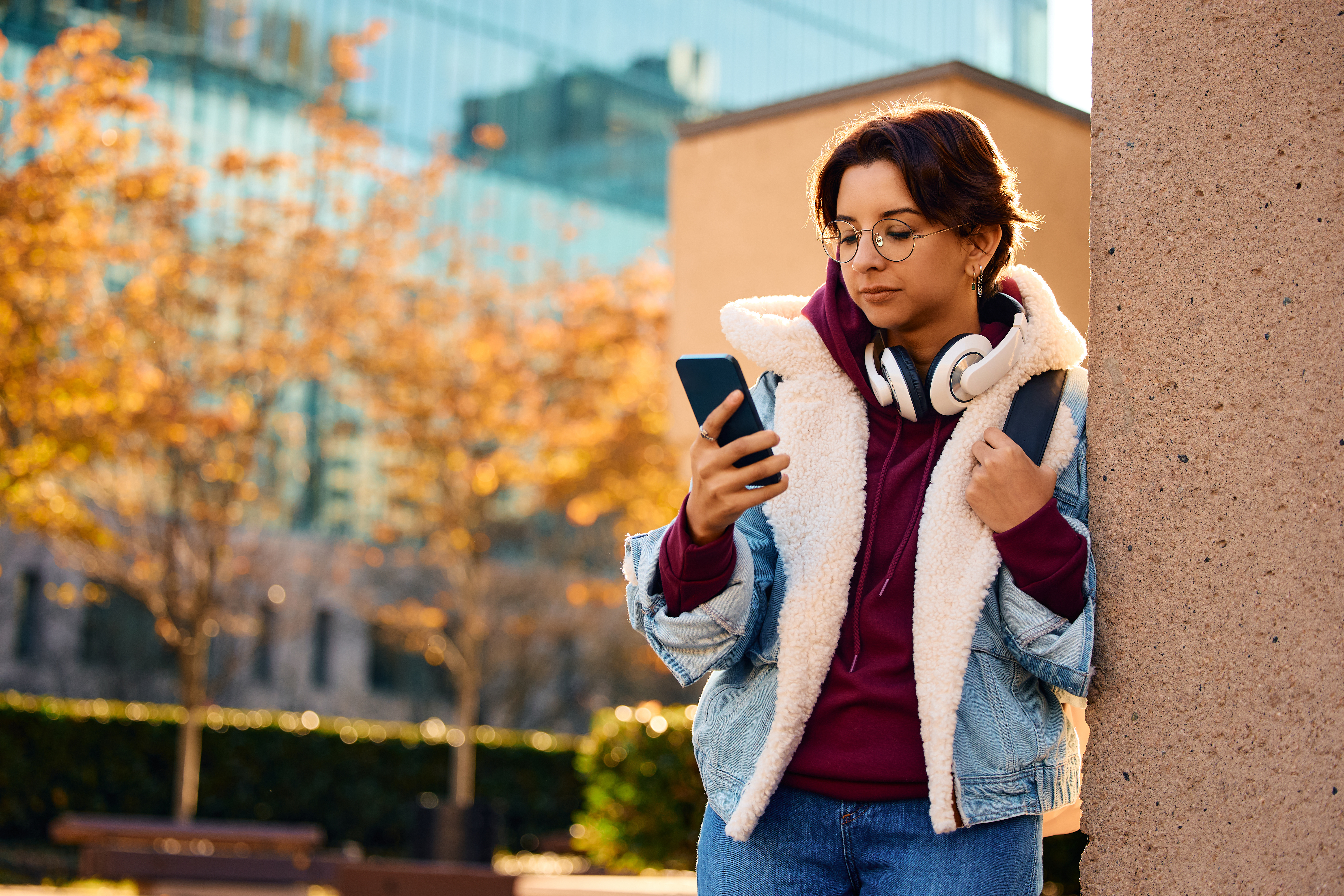 eine Studentin mit Smartphone in der Hand lehnt an einer Wand