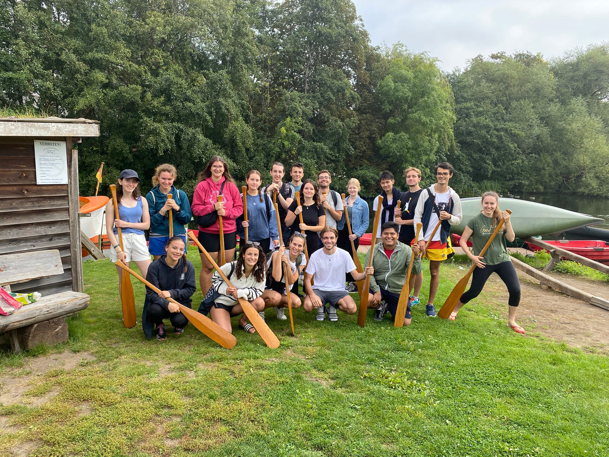 Eine Gruppe von Studierenden steht mit Paddeln an einem Gewässer