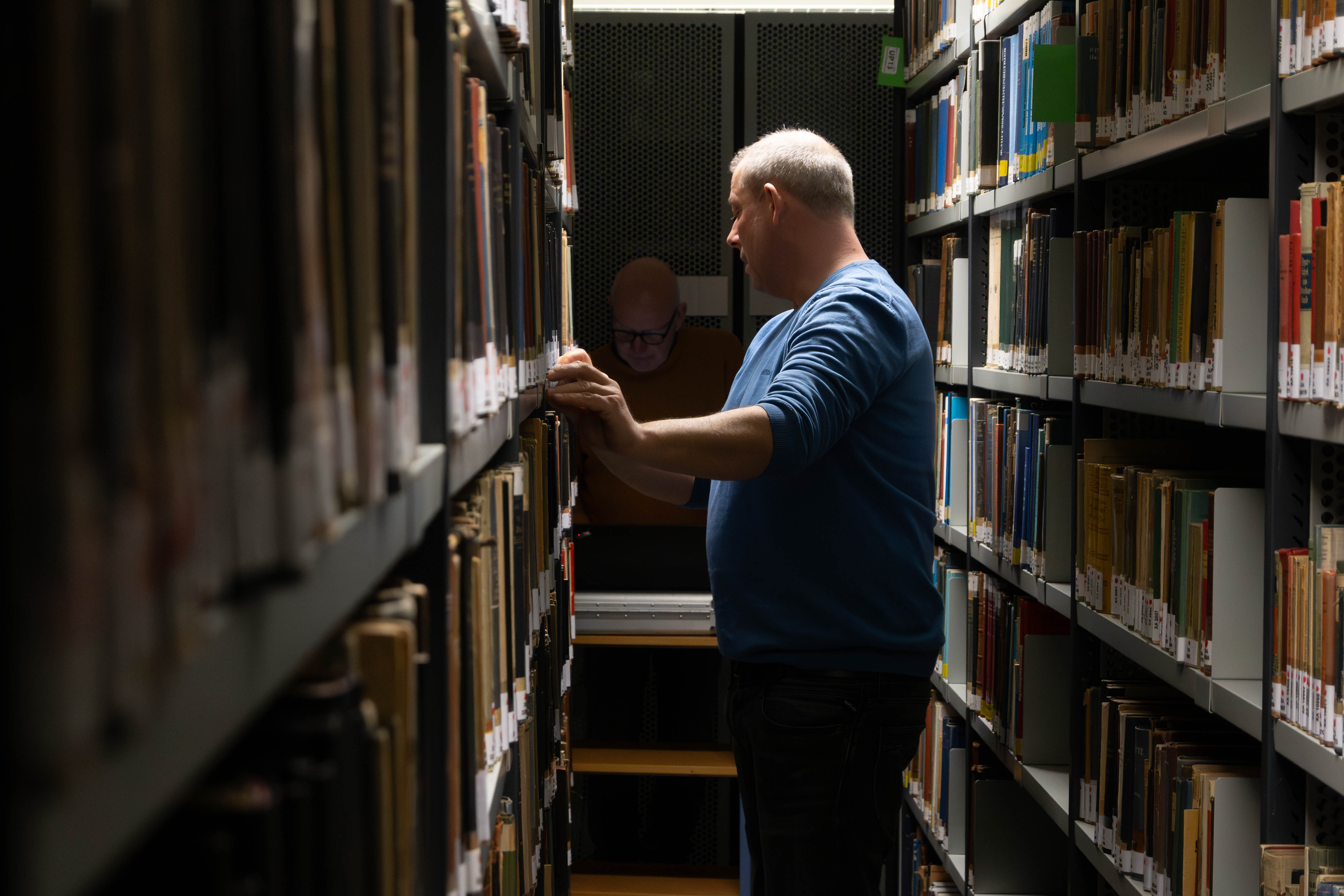 Mann zwischen Regalreihen voller Bücher.