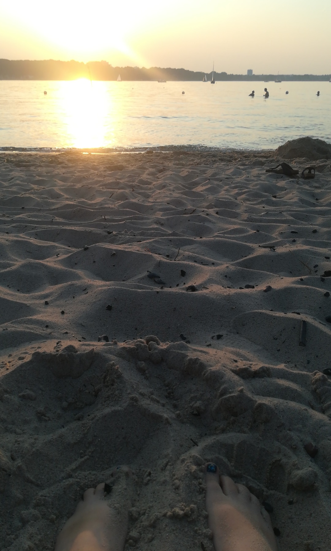 Sandstrand im Vordergrund, Wasser und der Sonnenuntergang im Hintergrund des Bildes.