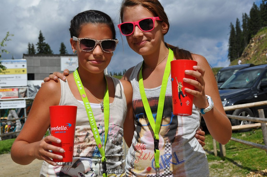 Zwei Mädchen mit bunten Sonnenbrillen und roten Trinkbechern posieren für die Kamera.