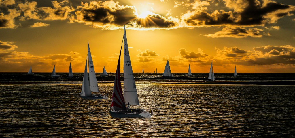 Eine vielzahl an Segelbooten schippernd vor einem goldenen Sonnenuntergang.