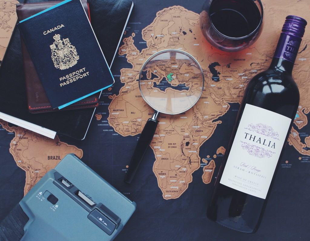 Auf einer Landkarte liegt eine Lupe, eine Flasche Wein und Reisedokumente.