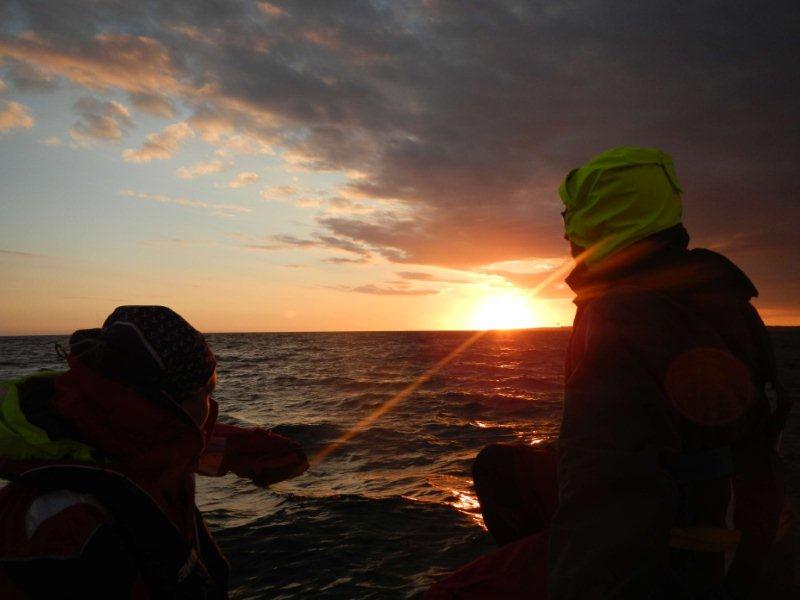 Zwei Männer segeln dem Sonnenuntergang entgegen.